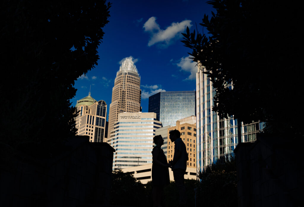 couple holding hands with buildings behind them in romare beardon park charlotte