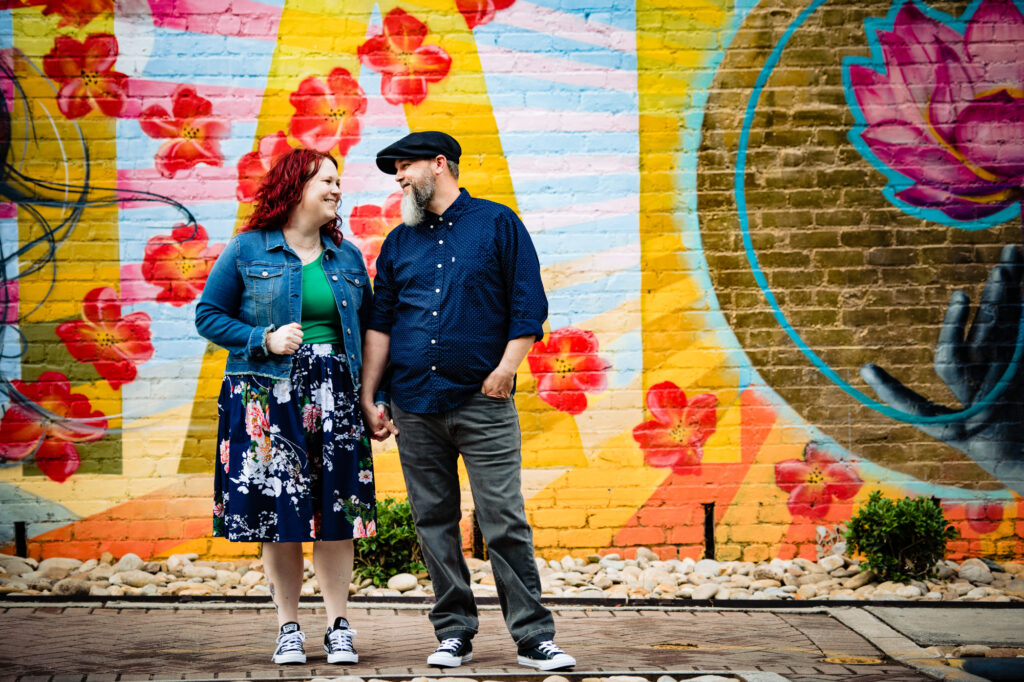 couple holding hands in front of colorful wall at Noda Charlotte North Carolina